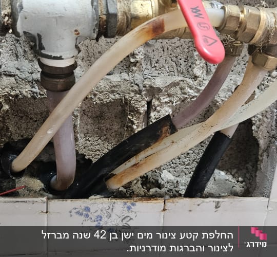 צינורות מים עם ברז אדום בקיר חשוף